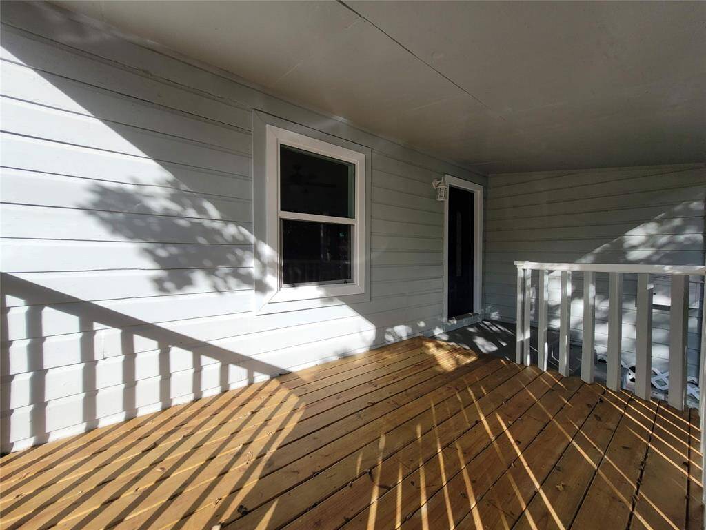 A cozy, covered wooden porch with white railings, light gray siding, and a single window, offering a welcoming entryway and outdoor space.