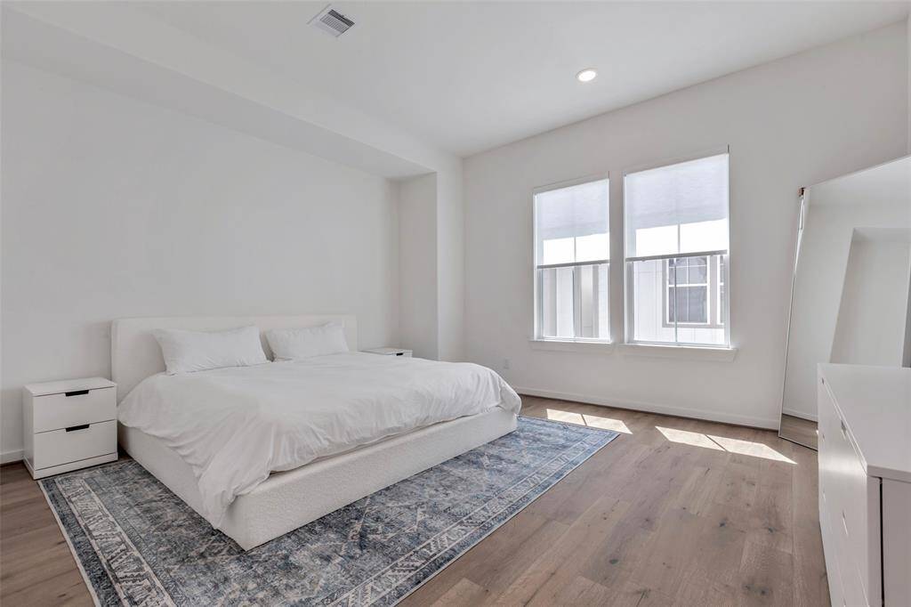 Welcome to the main bedroom, where large glass windows flood the space with natural light, highlighting the beautiful wooden floors and creating a bright, airy atmosphere.