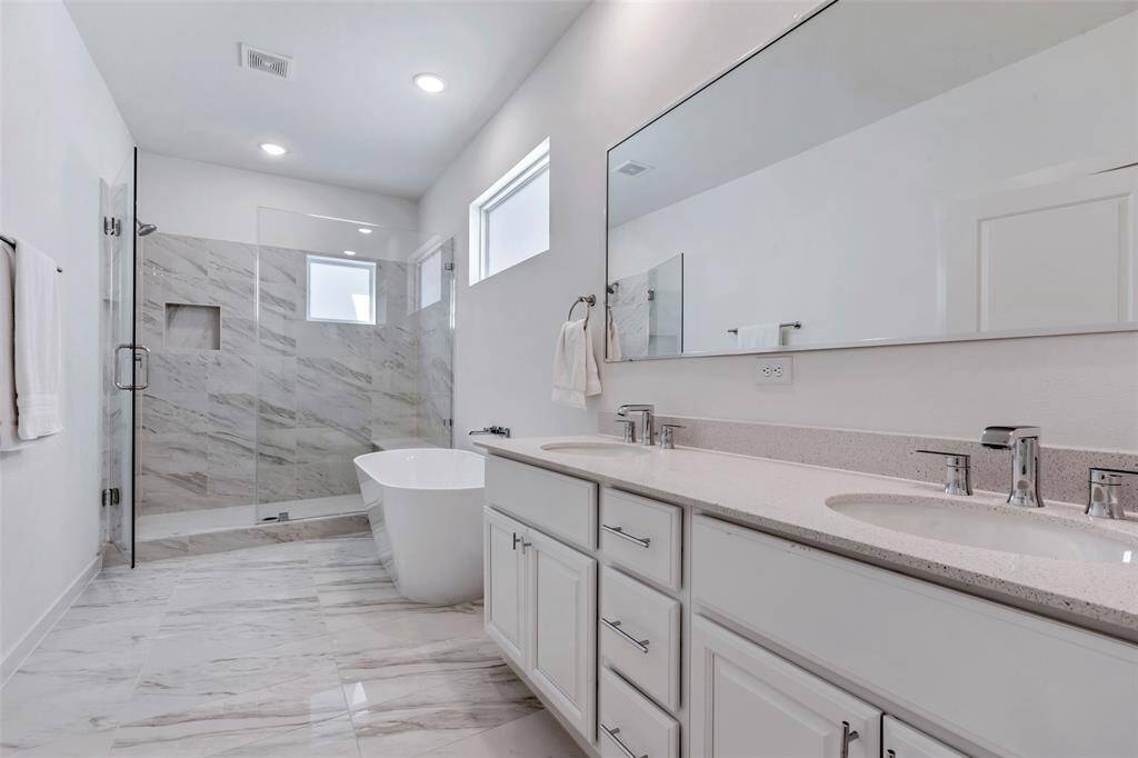 The main bathroom features stunning tiled floors, double sinks, a separate tub and shower, and an expansive vanity mirror—combining style and functionality for a luxurious feel.