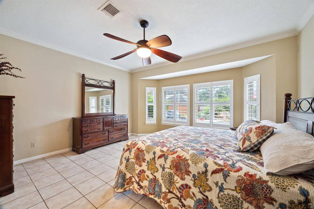 AS YOU STEP INTO THE PRIMARY SUITE, YOU NOTICE THE STUNNING VIEWS THROUGH THE CUSTOM SHUTTERS OF BACK YARD BEAUTY, CERAMIC TILE, CROWN MOLDING, AND CEILING FAN