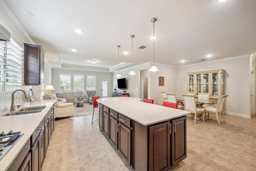 This open-concept living area features a modern kitchen with a large island, ample counter space, and dark cabinetry. It flows into a cozy living room with natural light from large windows. The adjacent dining area includes elegant seating and a display cabinet, perfect for entertaining.