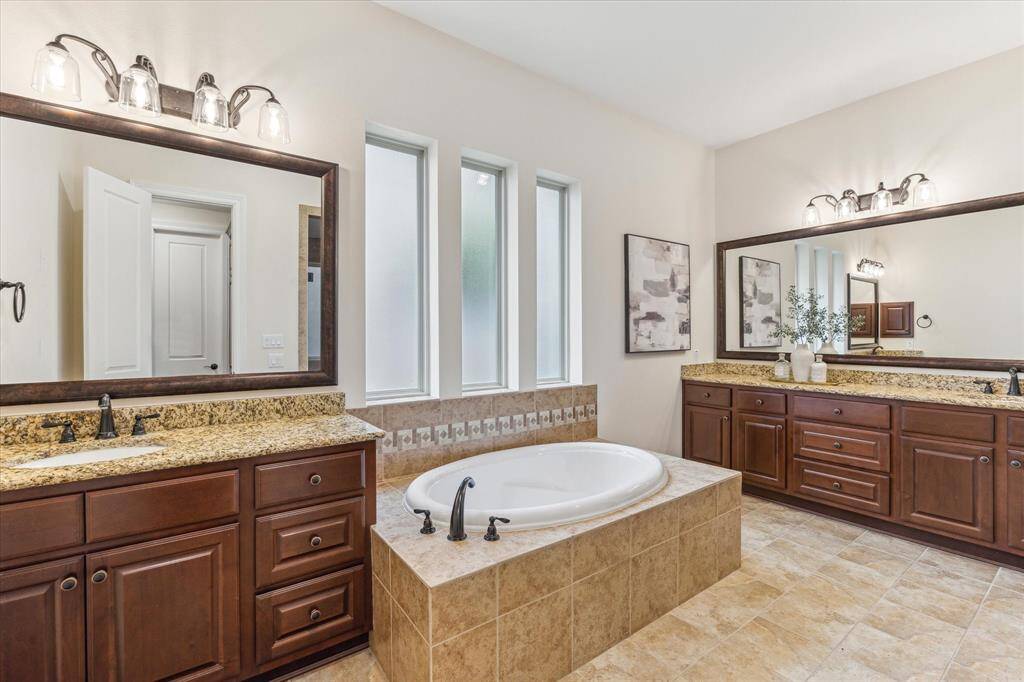 This beautifully designed primary bath showcases rich wood cabinetry with functional stacked drawers, a luxurious soaking tub, and framed mirrors that add a touch of sophistication. Pretty windows invite natural light, while rubbed bronze fixtures complete the space with timeless charm.
