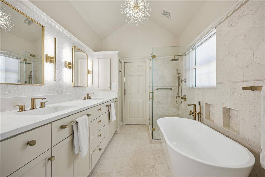 Recently renovated primary bathroom with honed travertine walls, double sinks, glass enclosed shower and free standing soaking tub. Wall behind the sinks is clad with mother of pearl tile.