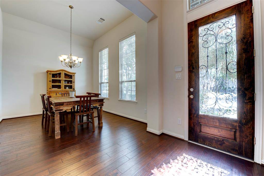 This inviting dining area features rich hardwood floors and a charming chandelier. Natural light streams through two large windows, while a decorative glass front door adds elegance and warmth to the space