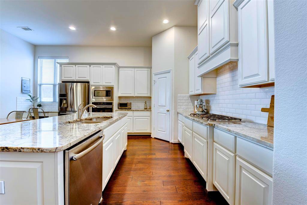 This modern and well designed kitchen features elegant white cabinetry, granite countertops, stainless steel appliances and a subway style backsplash. It has a spacious island with a built-in sink, hardwood flooring, and ample natural light. Perfect for modern living and entertaining!