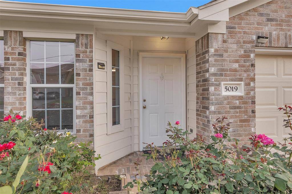 Charming front entrance with elegant brickwork and vibrant rose bushes, inviting you home.