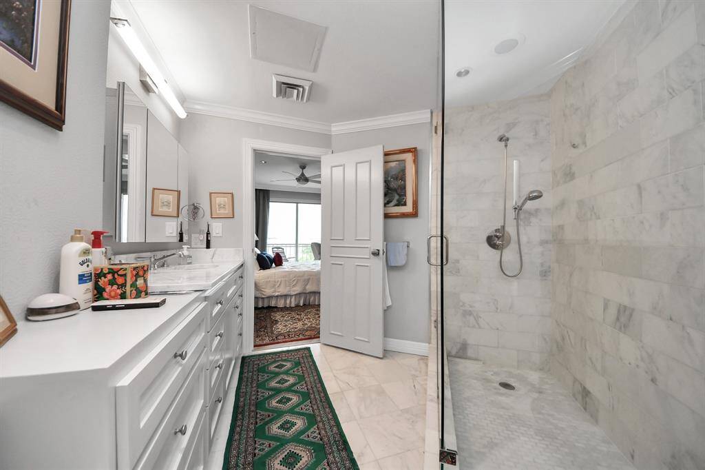 Extra large bathroom with a spacious marble-tiled shower and a dual-sink vanity. The room is bright and leads into a bedroom, offering a cohesive and stylish design.