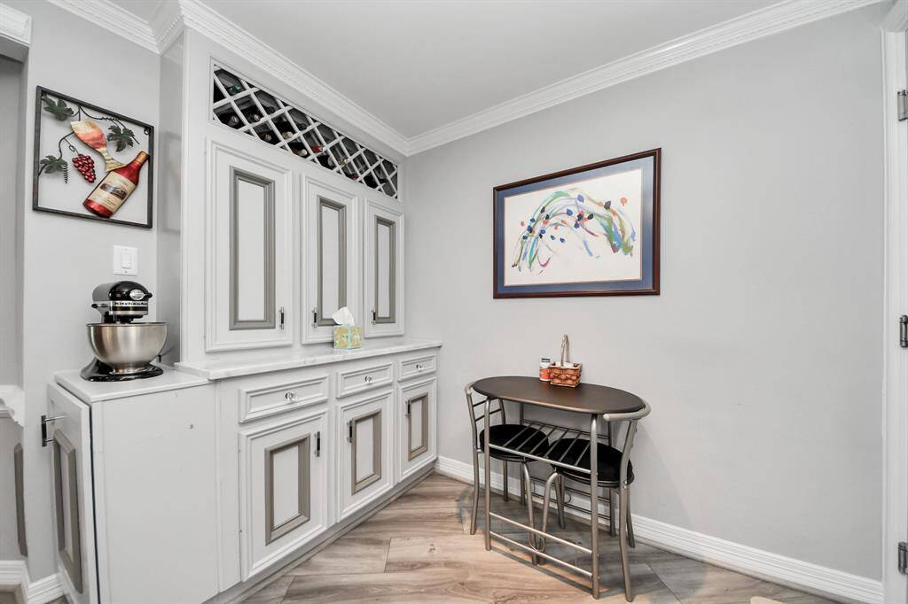 A cozy corner with a built-in cabinet featuring wine storage, unique built it appliance garage and a kitchen table area. The space is bright and stylish with light-colored walls and a touch of artistic flair.