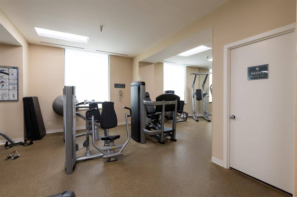 This well-maintained tennis court surrounded by lush greenery, perfect for sports enthusiasts. The court is located in a residential area with nearby houses, offering a suburban feel.