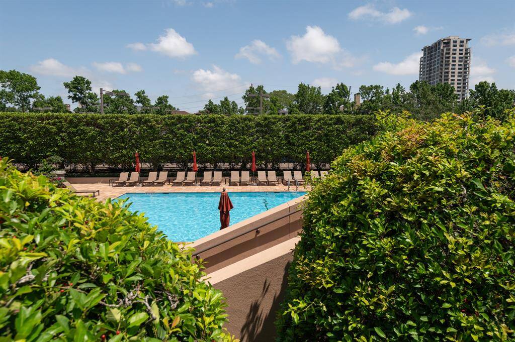 This showcases a serene outdoor pool area surrounded by lush greenery, offering a private and tranquil setting. Ideal for relaxation and leisure, the space features multiple lounge chairs and umbrellas, perfect for enjoying sunny days.