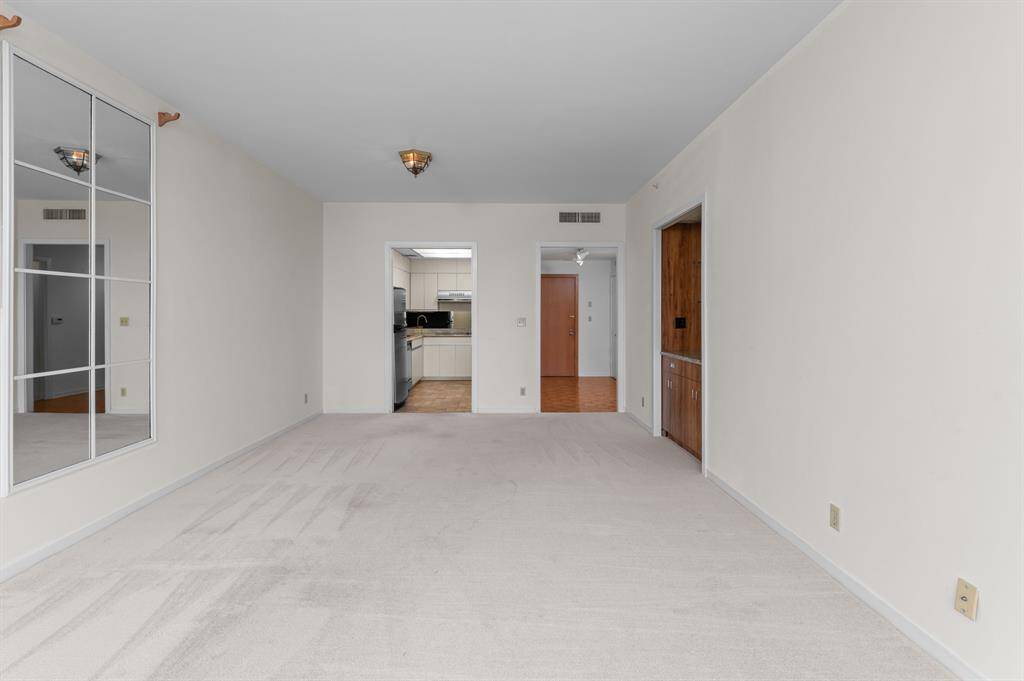 This room features neutral walls and carpeting, a ceiling fan, and access to a hallway with a glimpse of a bathroom. It offers a clean, blank canvas for personalization.