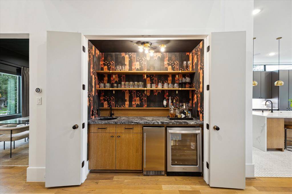 Tucked behind double doors, this statement wet bar dazzles with bold designer wallpaper, open shelving, and sleek under-counter appliances—bringing style and function to your entertaining space.
