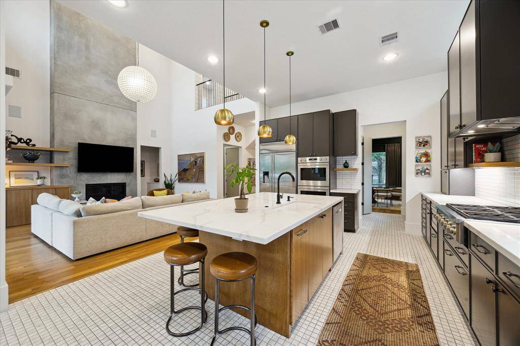 This showstopping kitchen seamlessly integrates into the open-concept living space, anchored by a waterfall-edge island, rich wood accents, and brass pendant lighting that adds a touch of luxe. Floor-to-ceiling cabinetry, professional-grade appliances, and designer tile flooring combine high function with modern flair.