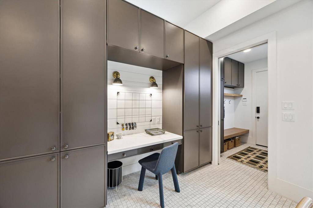 Tucked between custom cabinetry, this smartly designed office nook offers a bright and efficient workspace with built-in lighting, floating shelves, and seamless access to the mudroom.