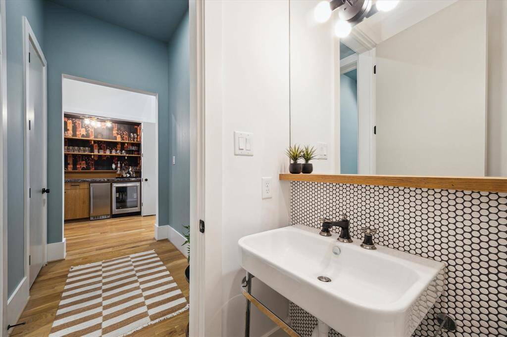This stylish powder room makes a bold statement with graphic penny tile, a sleek wall-mounted sink, and modern lighting—all thoughtfully tucked just off the vibrant wet bar area for added convenience.