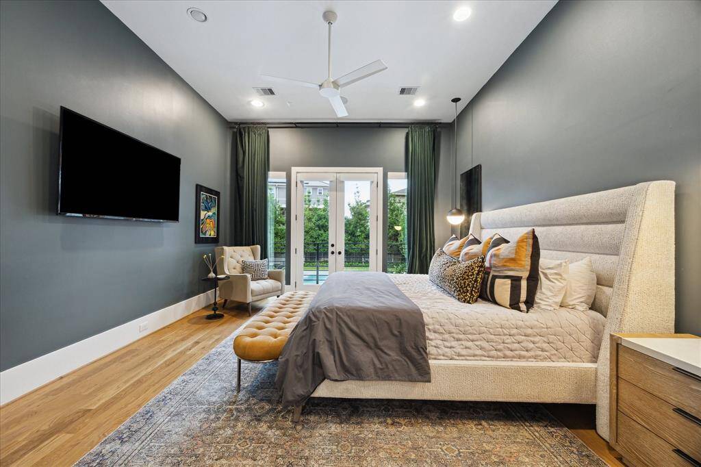 This serene primary suite exudes sophistication with rich wall tones, vaulted ceilings, and French doors that open to a tranquil poolside escape. Designer lighting, wide-plank wood floors, and layered textures create a luxurious retreat that feels both modern and timeless.