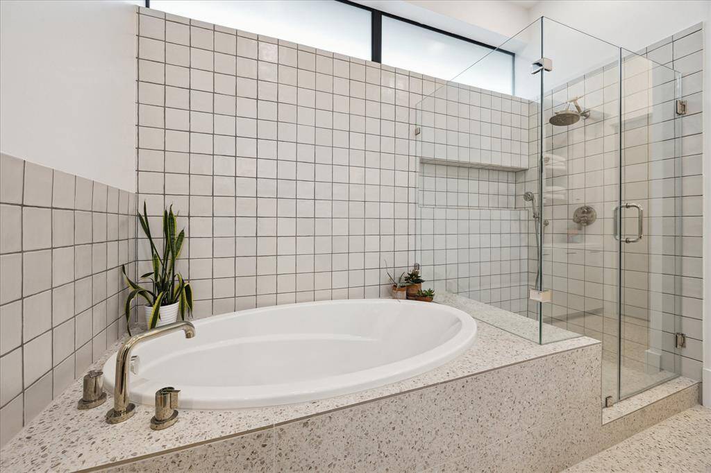 This contemporary primary bath features a soothing soaking tub set in terrazzo tile beside a frameless glass shower, all wrapped in handcrafted square tile for a clean, modern aesthetic. A clerestory window softly filters in natural light, enhancing the tranquil, spa-like ambiance.