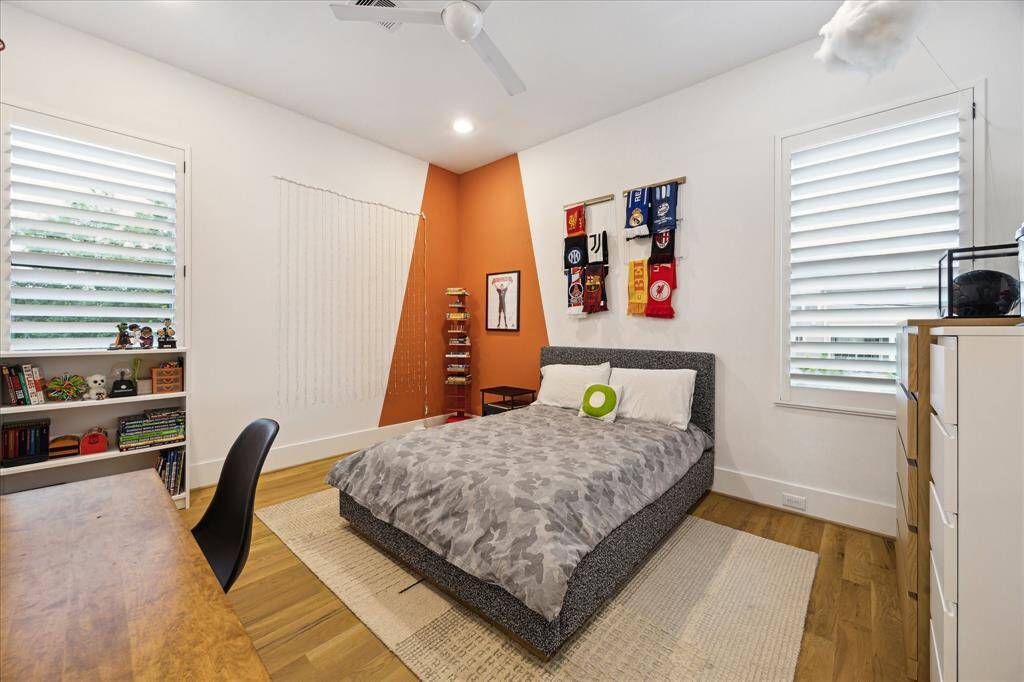 This bright and playful secondary bedroom features wide-plank wood floors, custom window shutters, and bold accent wall details that add personality and charm to the space.