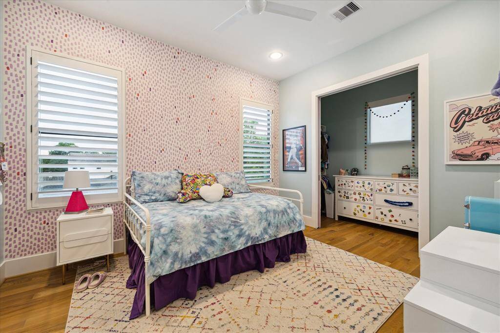 Bursting with personality, this vibrant secondary bedroom features playful patterned wallpaper, wide-plank wood floors, and custom window shutters that filter in natural light. A cozy sleeping nook and cheerful décor create a whimsical yet functional space perfect for rest and creativity.