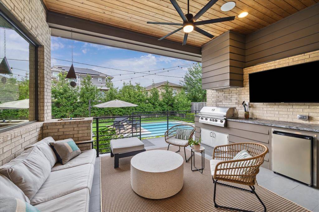 Framed by a warm wood ceiling and enhanced by a sleek built-in grill station with granite countertops, this covered outdoor lounge offers the ultimate in alfresco entertaining—complete with a beverage fridge, mounted TV, and captivating pool views just beyond.