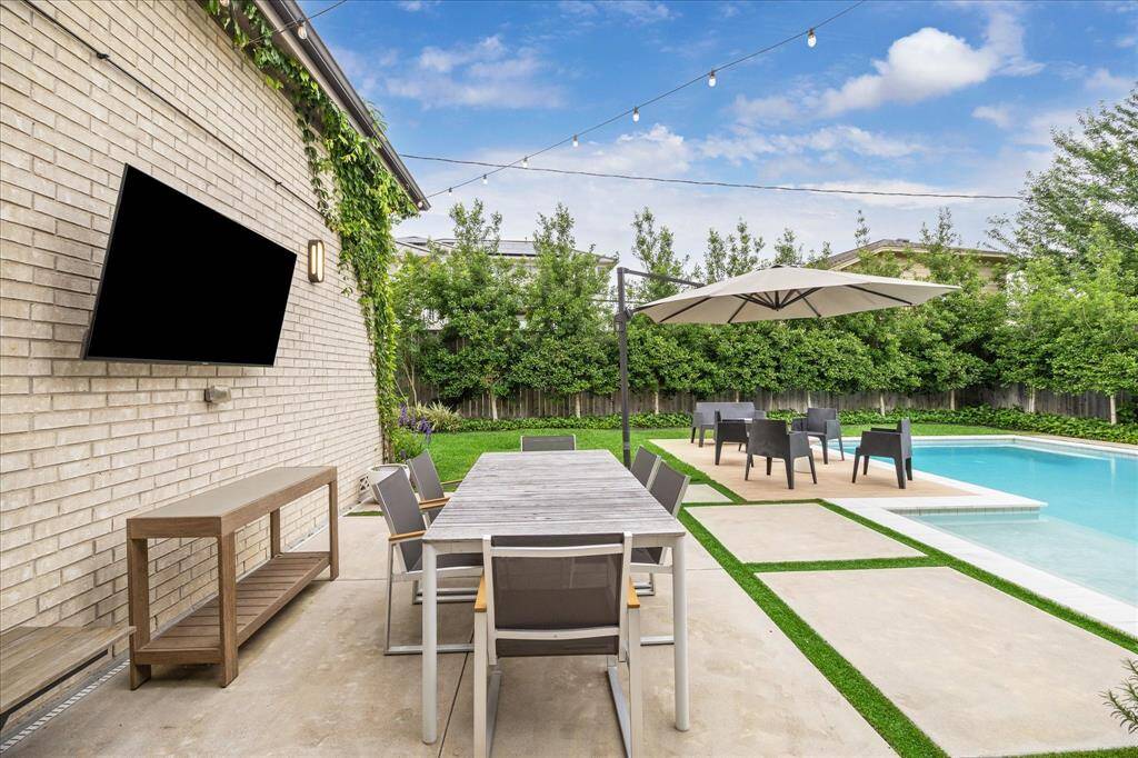 Surrounded by lush greenery and set beneath twinkling café lights, the poolside dining area offers a stylish al fresco setting complete with a mounted TV and ample seating—ideal for casual meals, entertaining, or enjoying a quiet evening under the stars.