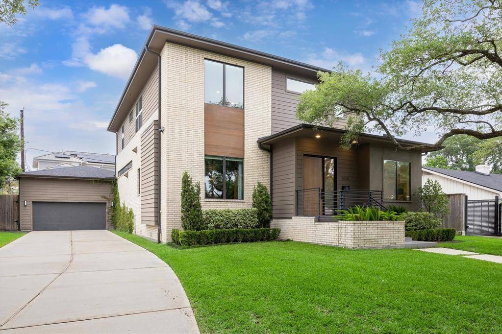 This striking contemporary residence makes a bold first impression with its clean architectural lines, warm brick and wood accents, and expansive windows that flood the interior with natural light. A manicured lawn, mature trees, and a sleek front porch with modern railing complete the inviting curb appeal.