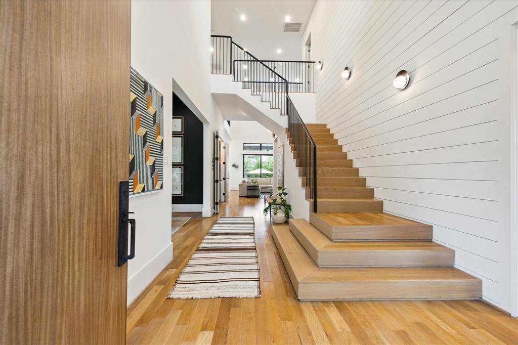 A bold architectural statement, this light-filled entryway showcases wide-plank oak floors, modern shiplap walls, and a sculptural open staircase that seamlessly blends form and function.