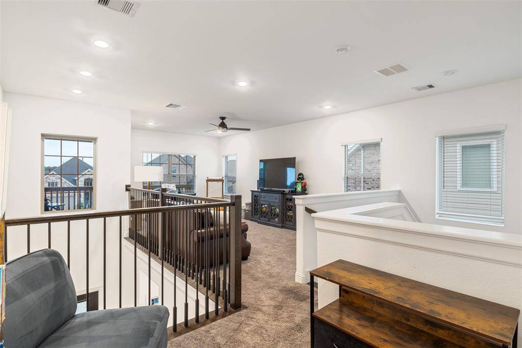 Spacious, carpeted upper-level living area with room for seating and ample natural light from multiple windows. The room features space for a modern entertainment setup and overlooks the lower floor with an elegant railing.
