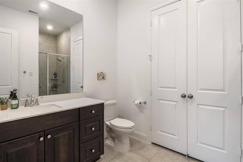 This bathroom attached to downstairs second bedroom features a modern design with a sleek vanity and ample storage space. It includes a large mirror, a walk-in shower with glass doors, neutral tile flooring and large two door closet.