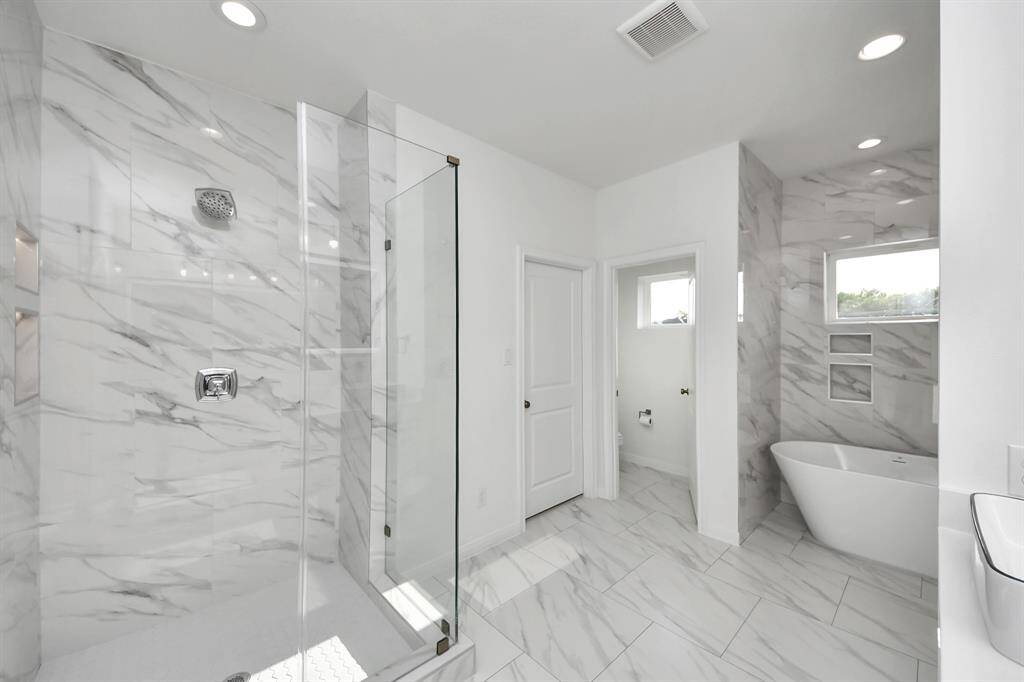 The main bathroom exudes both style and functionality, featuring a spacious stand up shower with a sleek ceramic tile and with glass doors and a freestanding bathtub perfect for soaking.