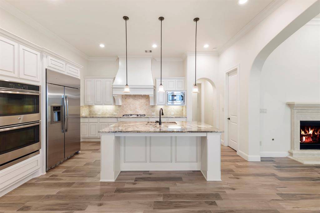 The chef’s kitchen impresses with a large granite island, Blanco sink, built-in refrigerator, double ovens, gas cooktop, and custom cabinetry.