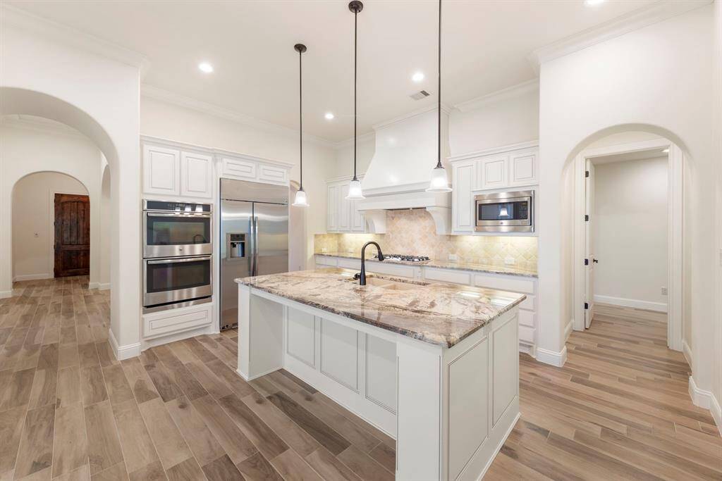 This gourmet kitchen showcases timeless elegance with white cabinetry, stainless steel appliances, a striking vent hood, and a granite island ideal for prep, dining, or entertaining.