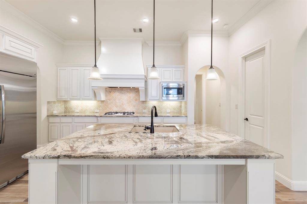 Centrally located and beautifully finished, the oversized granite island anchors this elegant kitchen, offering ample workspace, bar seating, and a stunning focal point beneath trio pendant lighting.