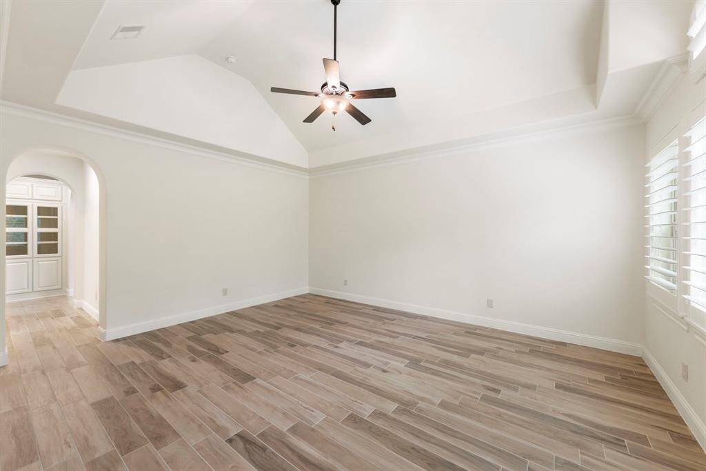 The serene primary suite features soaring vaulted ceilings, plantation shutters, and wood-look tile flooring, offering a peaceful retreat with direct access to a spa-inspired bath and walk-in closet. This photo has been virtually staged.