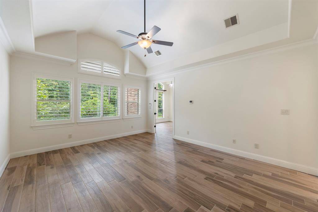Framed by plantation-shuttered windows and treetop views, the primary bedroom is a true sanctuary—complete with vaulted ceilings, rich tile flooring, and access to the adjacent sitting room.