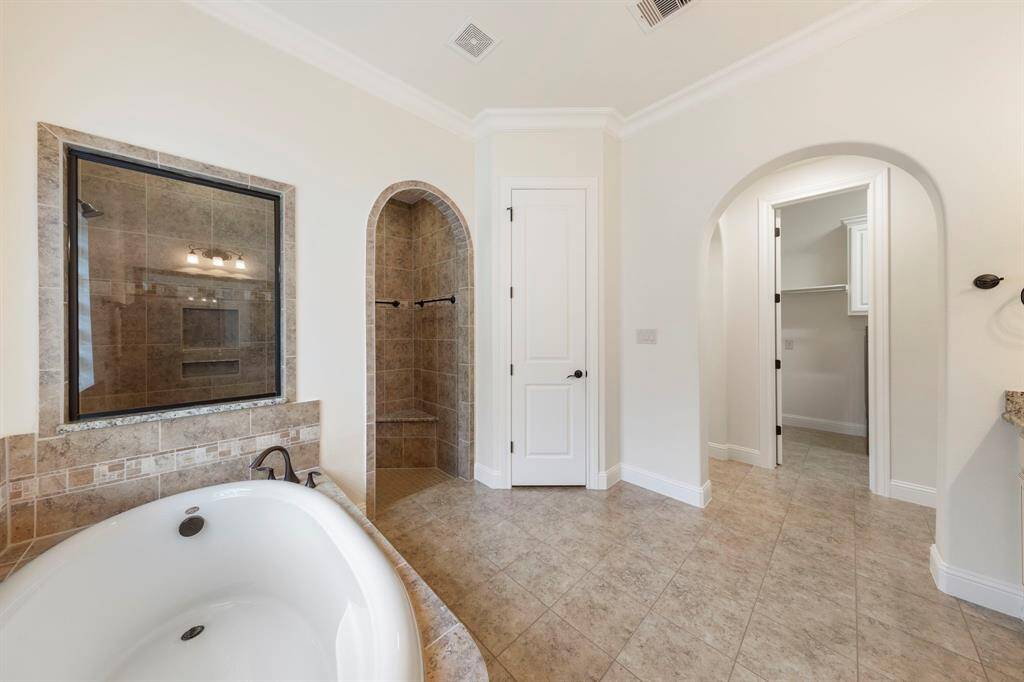 The primary bath offers a spacious walk-in shower with arched entry and bench seating, a deep soaking tub, and direct access to a generous walk-in closet.