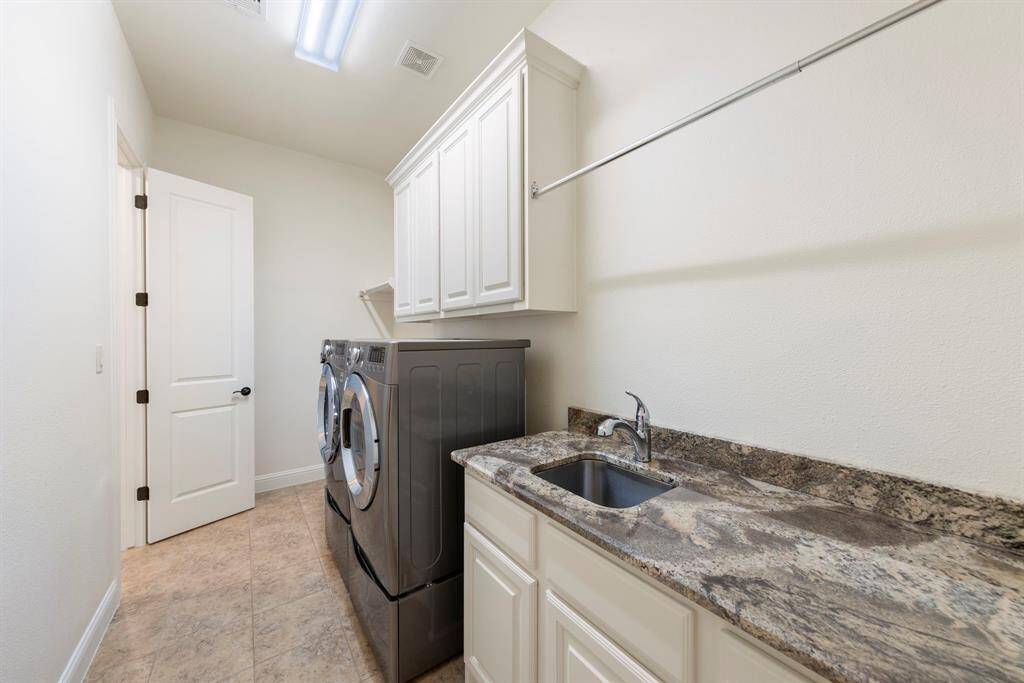 This well-appointed laundry room features granite countertops, a utility sink, upper cabinetry for storage, and direct access to the primary closet—designed for maximum efficiency and daily convenience. Washer & dryer convey.