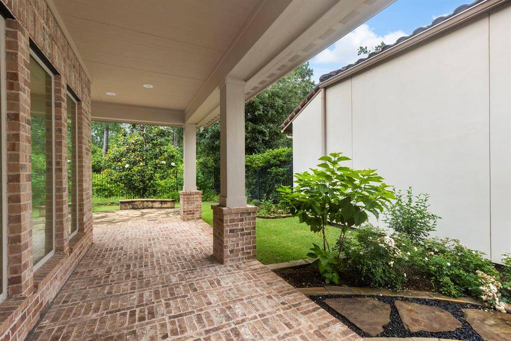This expansive covered patio offers a serene outdoor retreat with brick flooring, lush landscaping, and direct access to a private garden space.