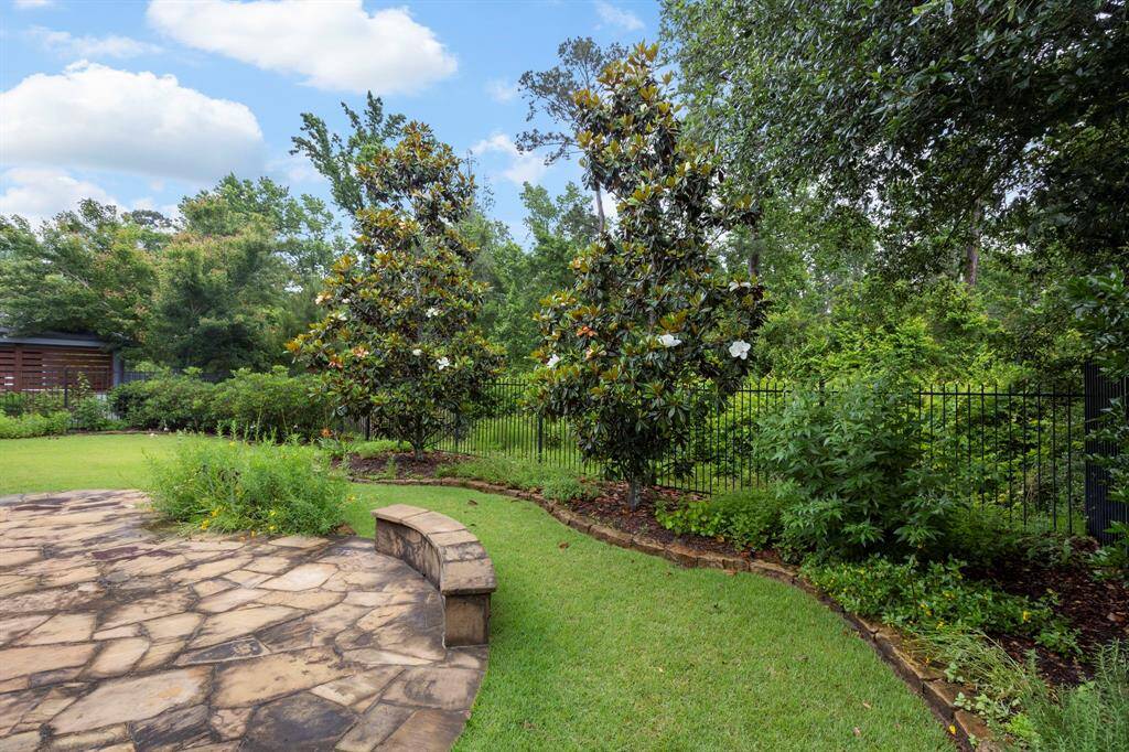 The backyard retreat features lush landscaping, flowering magnolia trees, and a stone patio with curved bench seating—perfect for peaceful mornings or relaxed outdoor gatherings.