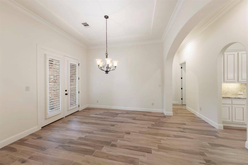 Bright and inviting, the formal dining room features elegant crown molding, wood-look tile flooring, and double French doors with plantation shutters that open to serene outdoor views. This photo has been virtually staged.