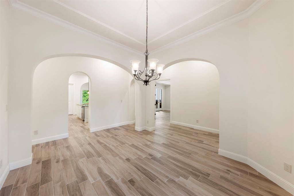 Graceful archways and rich wood-look tile flooring set the tone for timeless elegance in this open dining area, seamlessly connecting to the kitchen and living spaces.