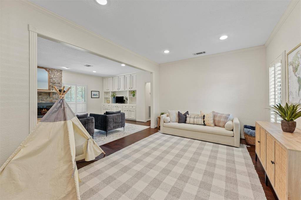 This formal living area features a cozy atmosphere with neutral tones, recessed lighting and plantation shutters. It opens into the family room. Natural light pours in through the windows, highlighting the room's inviting layout. Plenty of opportunities to use the space as a play area, office space or formal living!