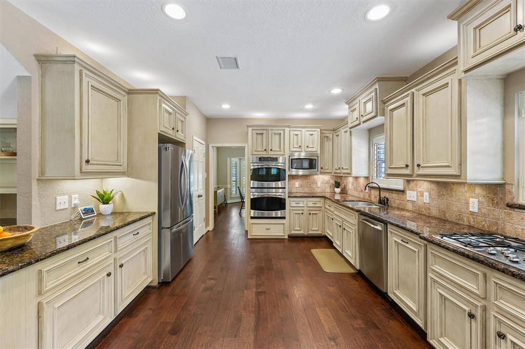 This chef's kitchen features elegant solid wood cabinetry, ample storage and cabinetry, granite countertops, and stainless steel appliances, including a double oven and gas cooktop. The hardwood floors and recessed lighting create a warm, inviting atmosphere.