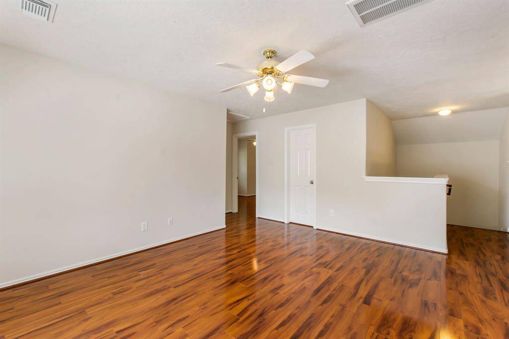 An additional view of the game room with a closet, laminate wood floors, a ceiling fan and fresh paint.