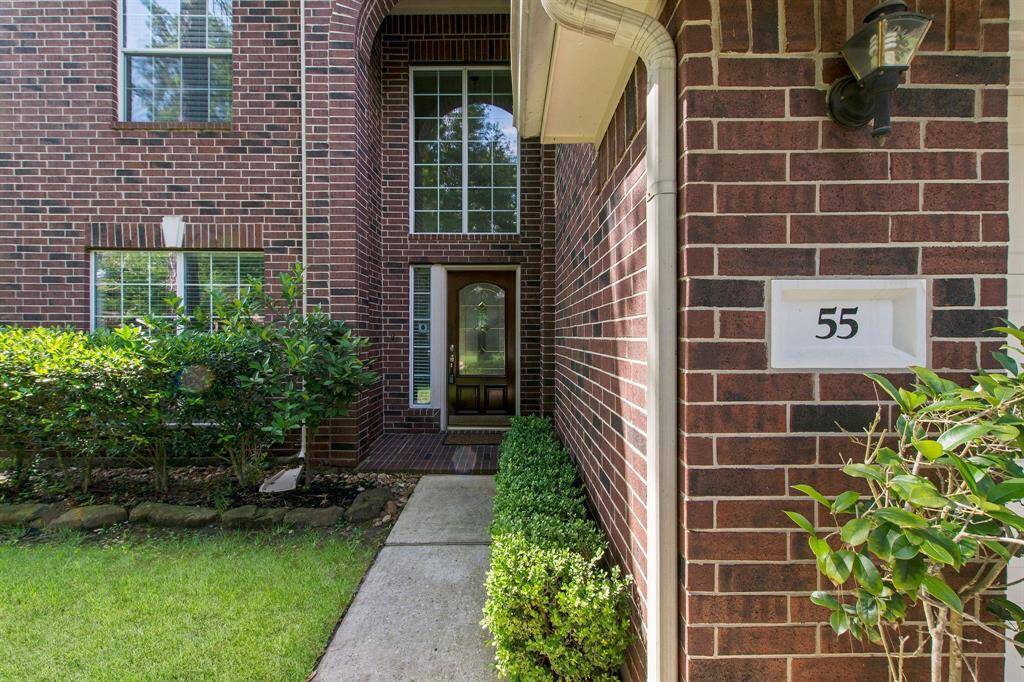 The traditional red brick home features manicured landscaping and wood lead glass door.