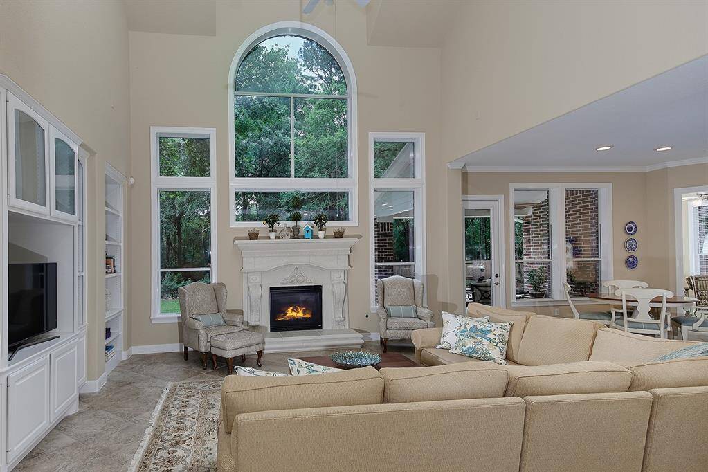 This spacious family room features a grand fireplace, high ceilings and a large arched window offering a view of lush greenery. The open layout flows into the casual dining space with ample natural light.