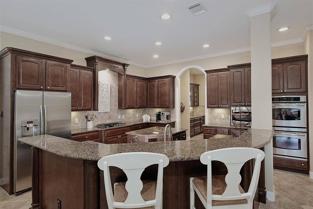 This kitchen features dark wood cabinetry for a more sophisticated look. Granite countertops, stainless steel appliances and breakfast bar. The area is well-lit with recessed lighting, creating a warm and inviting atmosphere.