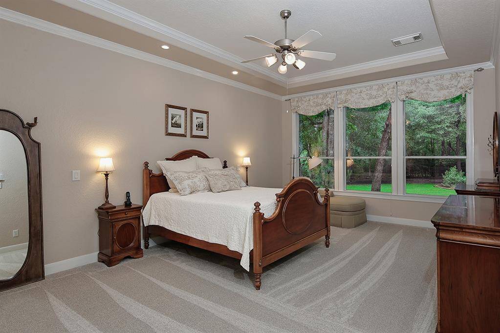 The spacious primary bedroom offers a serene view of lush greenery through expansive windows. Tray ceiling with molding is an upscale feature.