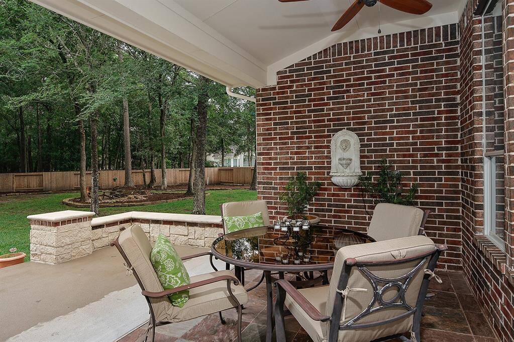 The covered patio with brick walls and a ceiling fan overlooks a well-maintained backyard with a wooden fence and lush greenery, offering a serene outdoor retreat.
