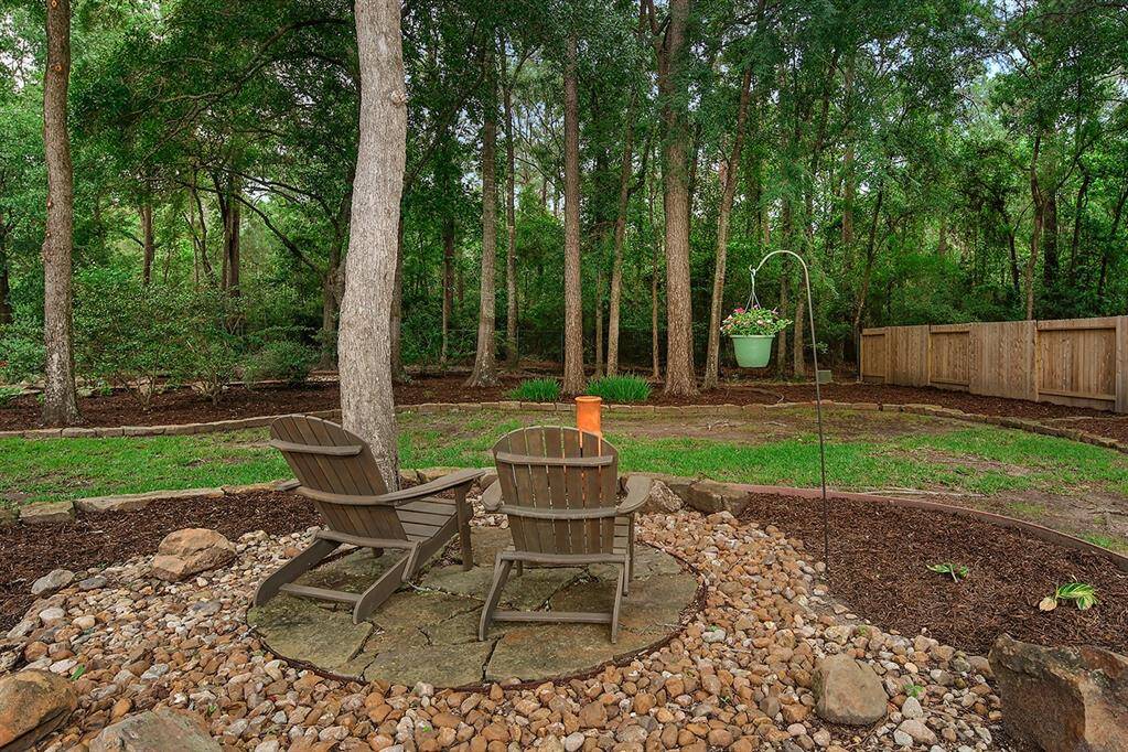 This backyard offers a serene, wooded setting with mature trees and a natural landscape. It features a cozy seating area on a stone patio, ideal spot for relaxation and enjoying nature.